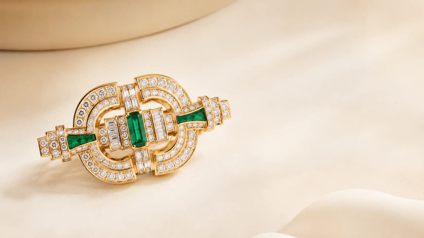 Gold and emerald jewellery on a warm ivory editorial background
